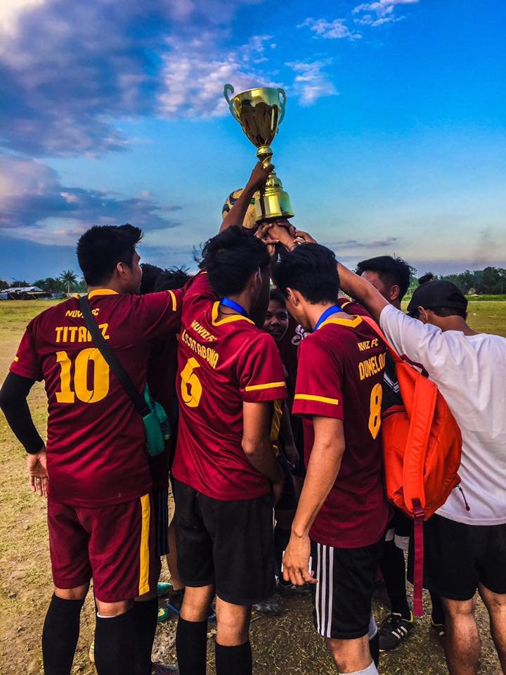 Nuviz Team football players in maroon jerseys celebrate victory by lifting a golden trophy together.