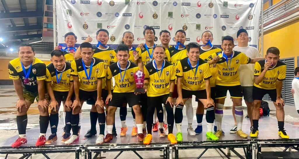 Dancalan FC men’s team in yellow jerseys posing on stage with medals and a championship trophy after winning a football tournament.