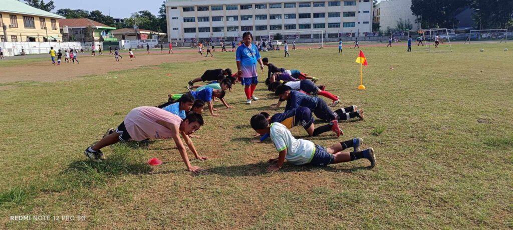 Young Cavalier FC players perform strength and conditioning exercises on a football field under the guidance of their coach during a weekend training session.