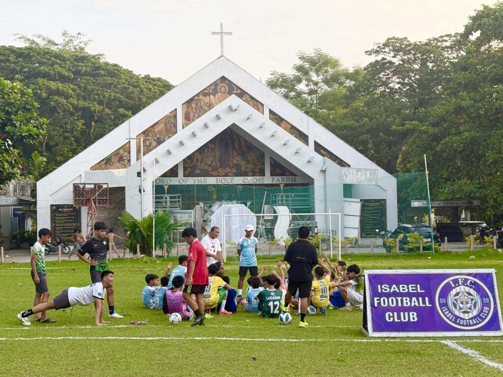 Children training with Isabel Football Club on a grassy field in front of Lord of the Holy Cross Parish in Iligan City.