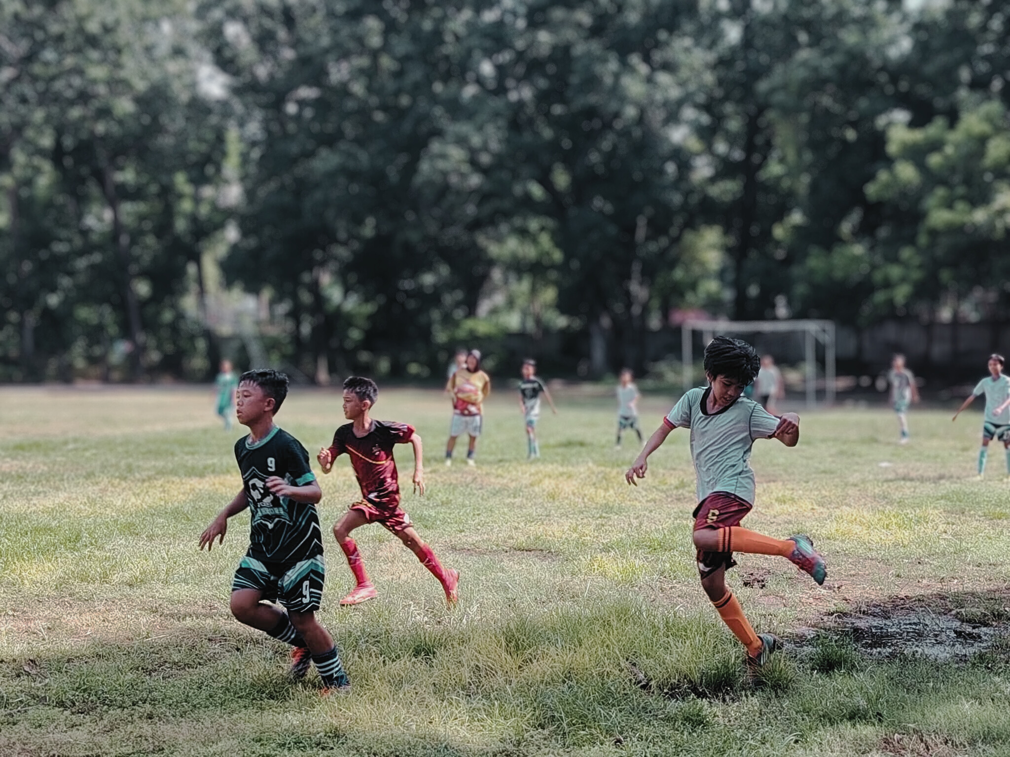 Young boys playing grassroots football during a community match on a grassy field in the Philippines.
