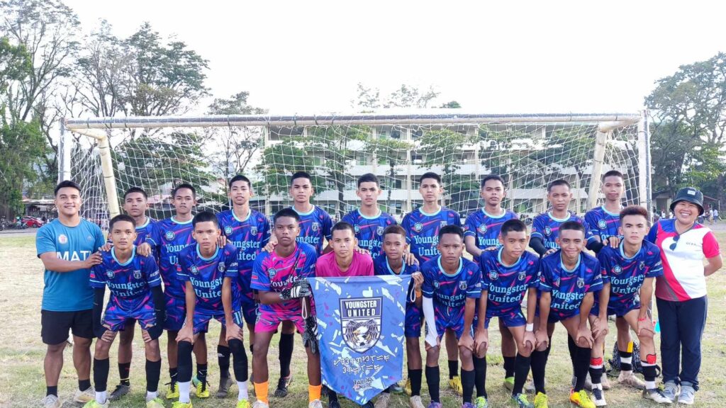Youngsters United Football Club players and coaches pose together in full team kit in front of a goalpost, holding the club banner on a football field in Gingoog City.