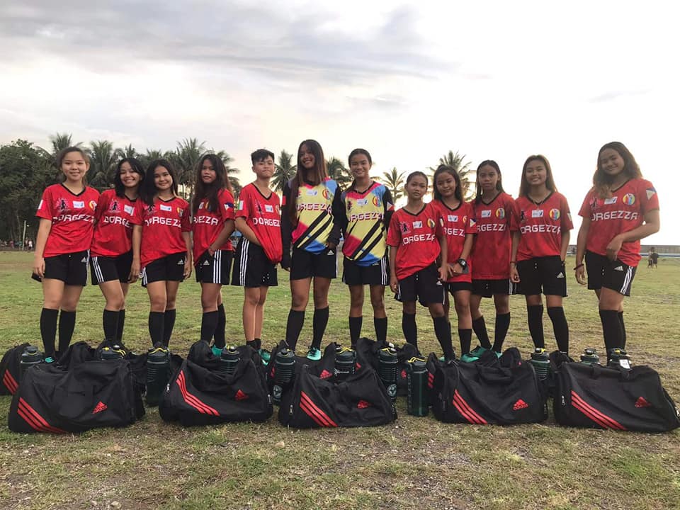 Young players from R. MCHEAVEN, a Philippine football club, preparing for a girls’ football training session on a grass field