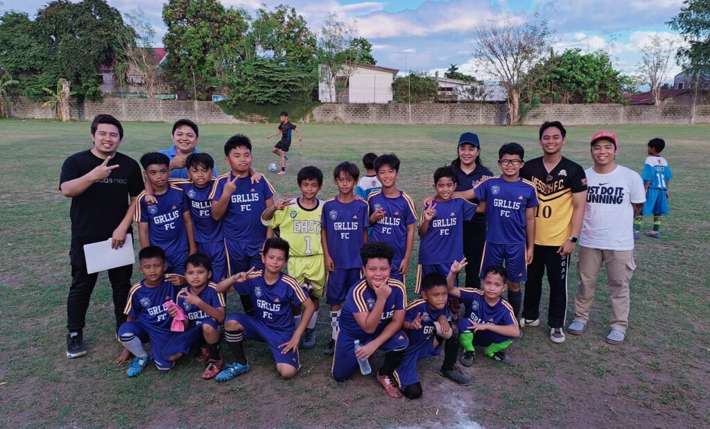 Young GRLLIS Football Club players and coaches in blue jerseys posing on a football field representing a grassroots Philippine Football Club.