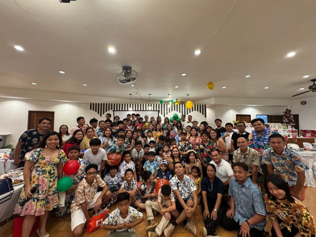 Group photo of Green Dragons FC players, families, and coaches celebrating together indoors with balloons and festive decorations in Tagbilaran City, Bohol.