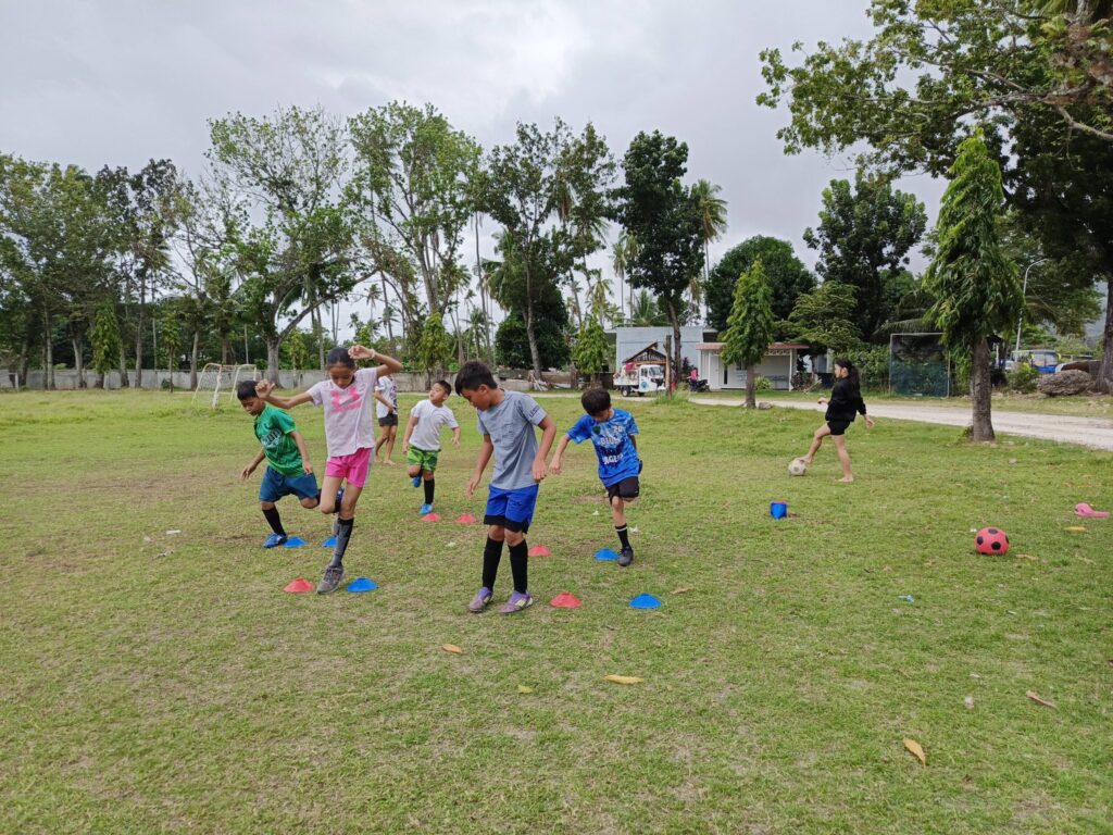 Young players from a Philippine Football Club doing cone drills during an outdoor football training session on a grass field.