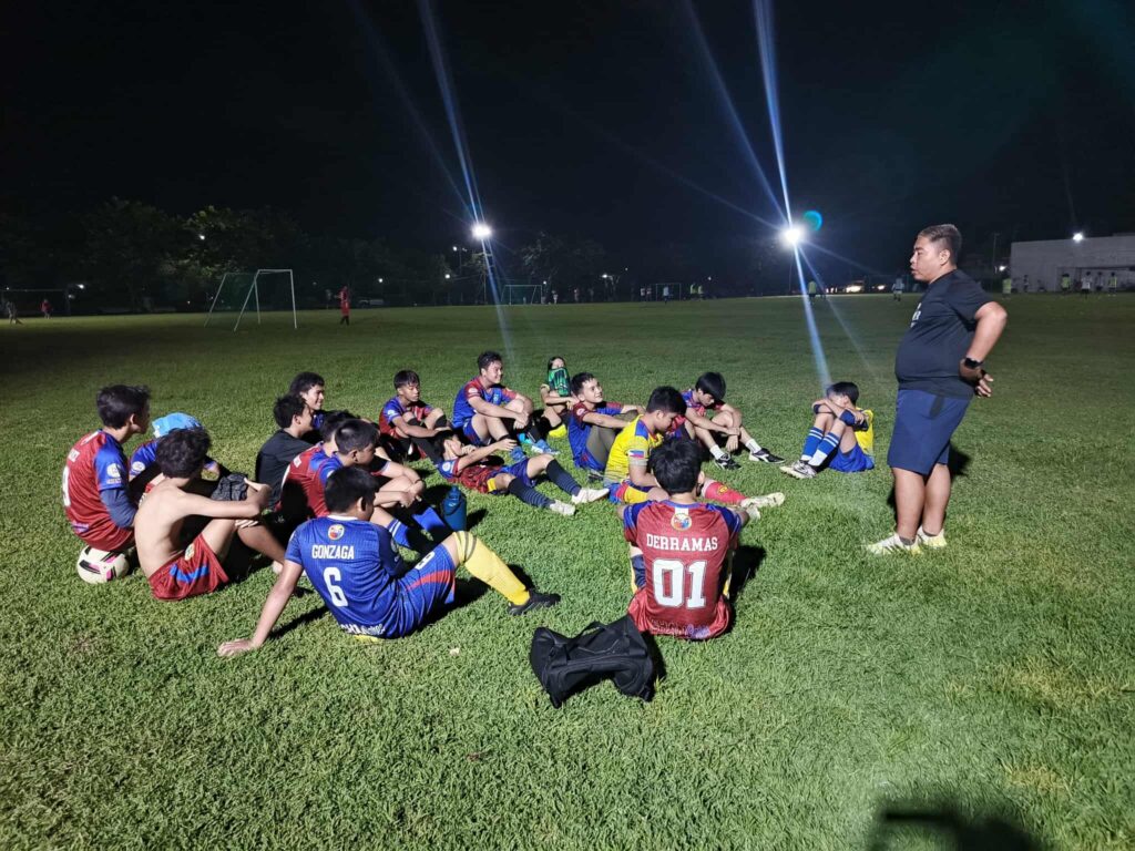 Coach leading young players in a night training session at Lapu-Lapu City Football Club, a grassroots Philippine Football Club developing youth talent.