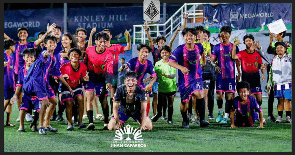 A joyful group of young footballers from EMA Bulacan Highlanders FC in purple and pink kits, celebrating on the pitch at McKinley Hill Stadium during the AIA 7's Football League.