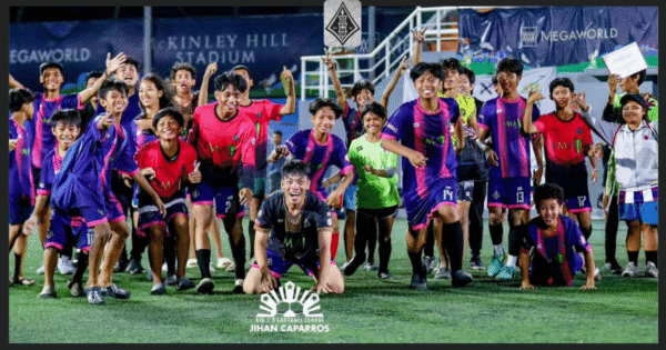 A joyful group of young footballers from EMA Bulacan Highlanders FC in purple and pink kits, celebrating on the pitch at McKinley Hill Stadium during the AIA 7's Football League.