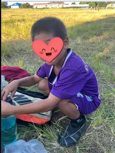 A young football player in a purple kit crouching on a grassy field beside his sports bag during football training.