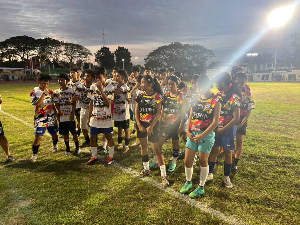 Young boys and girls from Spartan FC Calindagan gathered on a football field during a grassroots football event.