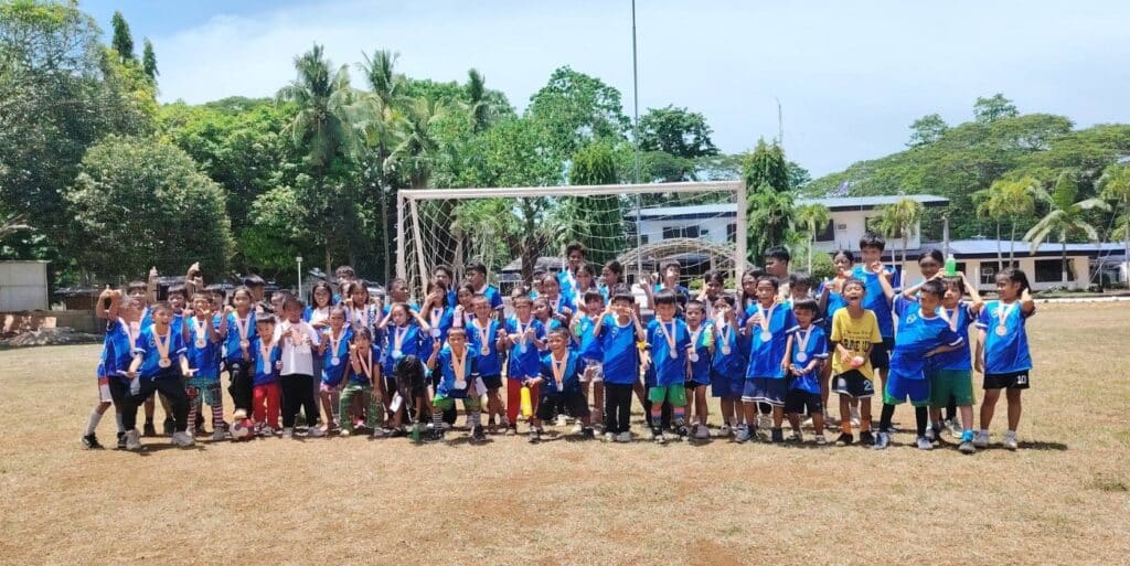 Young participants of the Kick It Futsal Summer Clinic posing with medals after completing a grassroots futsal training program in Puerto Princesa City, Palawan